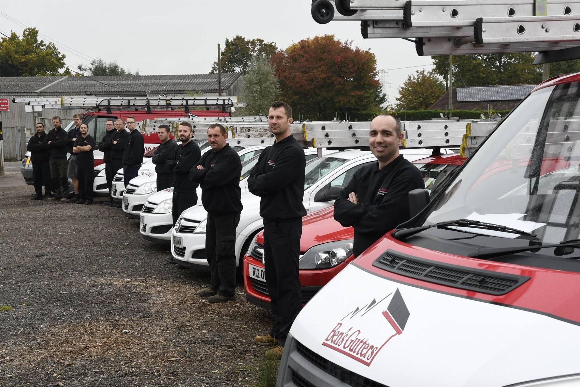 A team of uniformed workers stands in front of their vehicles, a van in the foreground.