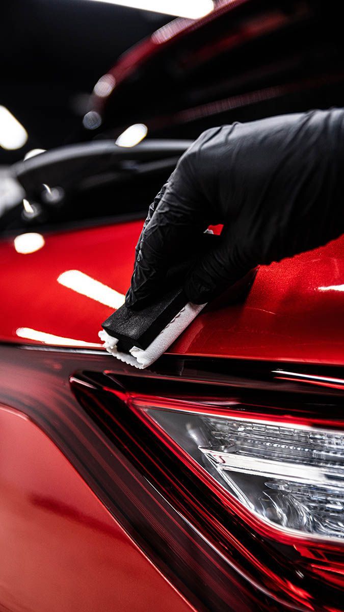 Gloved hand polishing the red paint of a car near the rear taillight