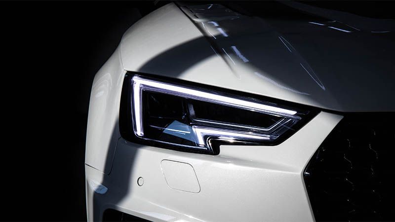 Close-up of a white car’s angular LED headlight and front grille in low light
