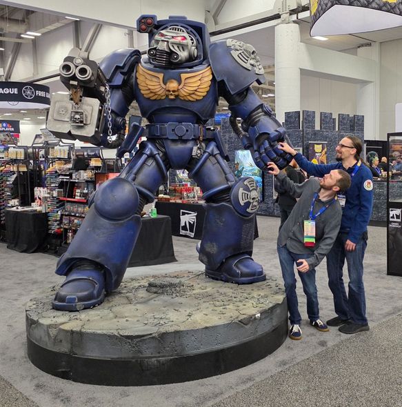 Child and adult posing beside a giant blue armored robot statue at a convention hall