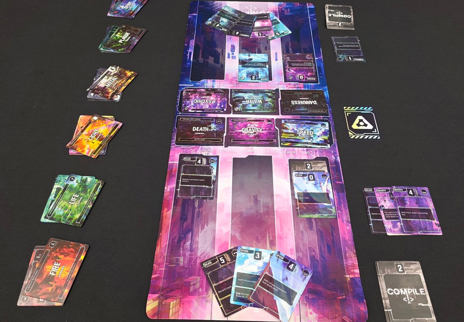 Colorful cards and game pieces arranged on a black tabletop around a central purple-blue game board.