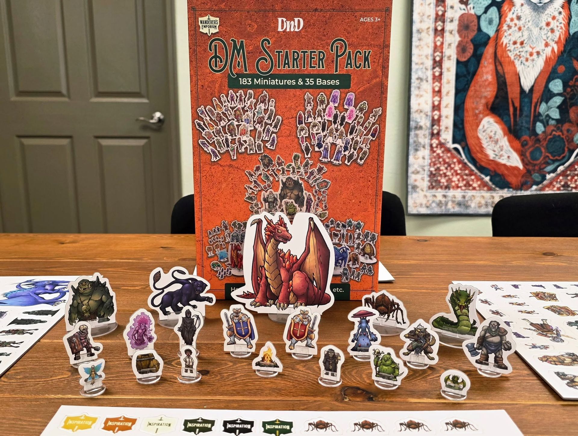 Board game setup with orange box art and many character standees on a table, plus cards laid out around them