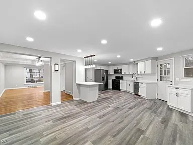 Bright open-plan kitchen and living area with gray floors, white cabinets, and hardwood flooring in adjacent room