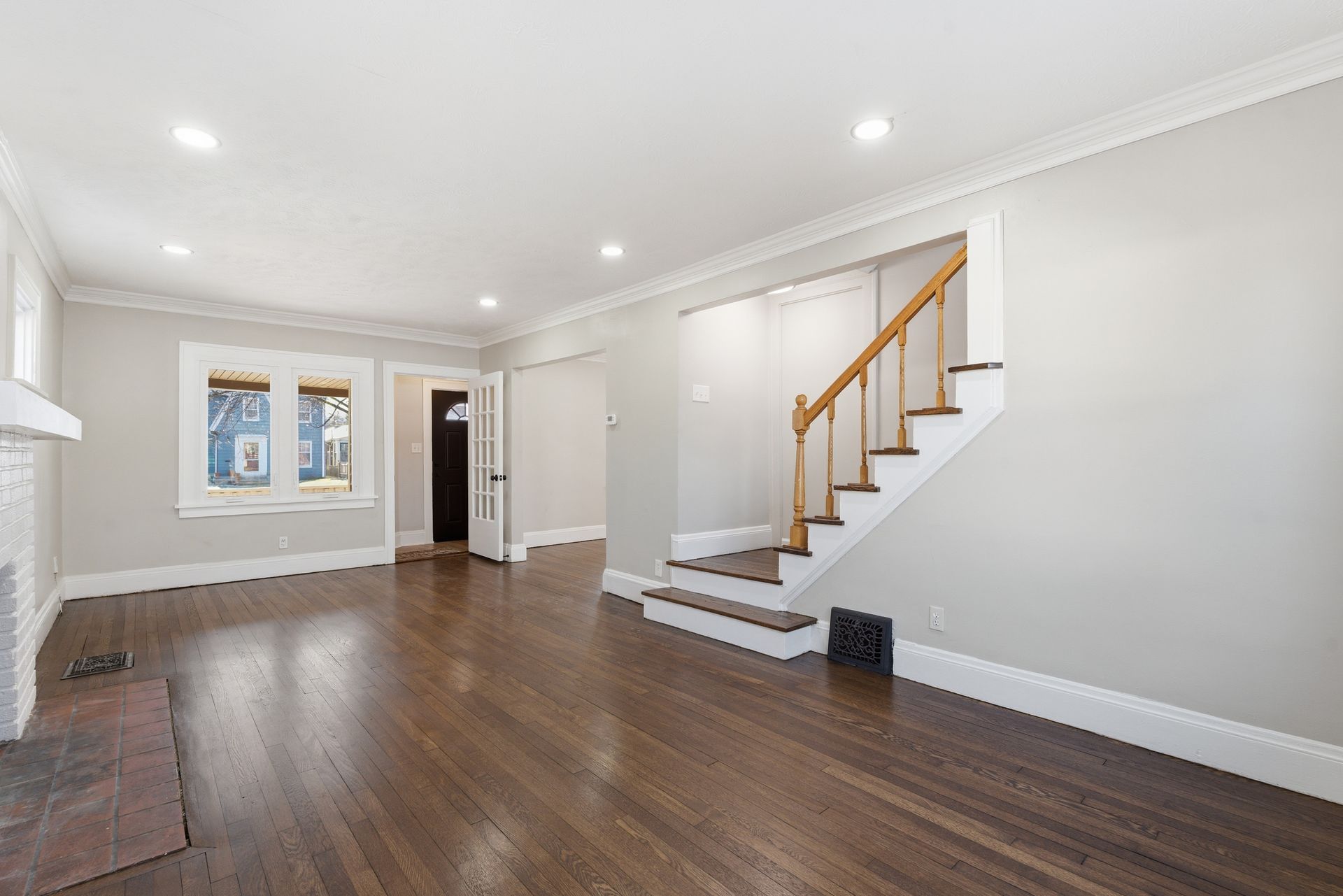 Empty white living room with dark hardwood floors, recessed lights, and a staircase with wood railing