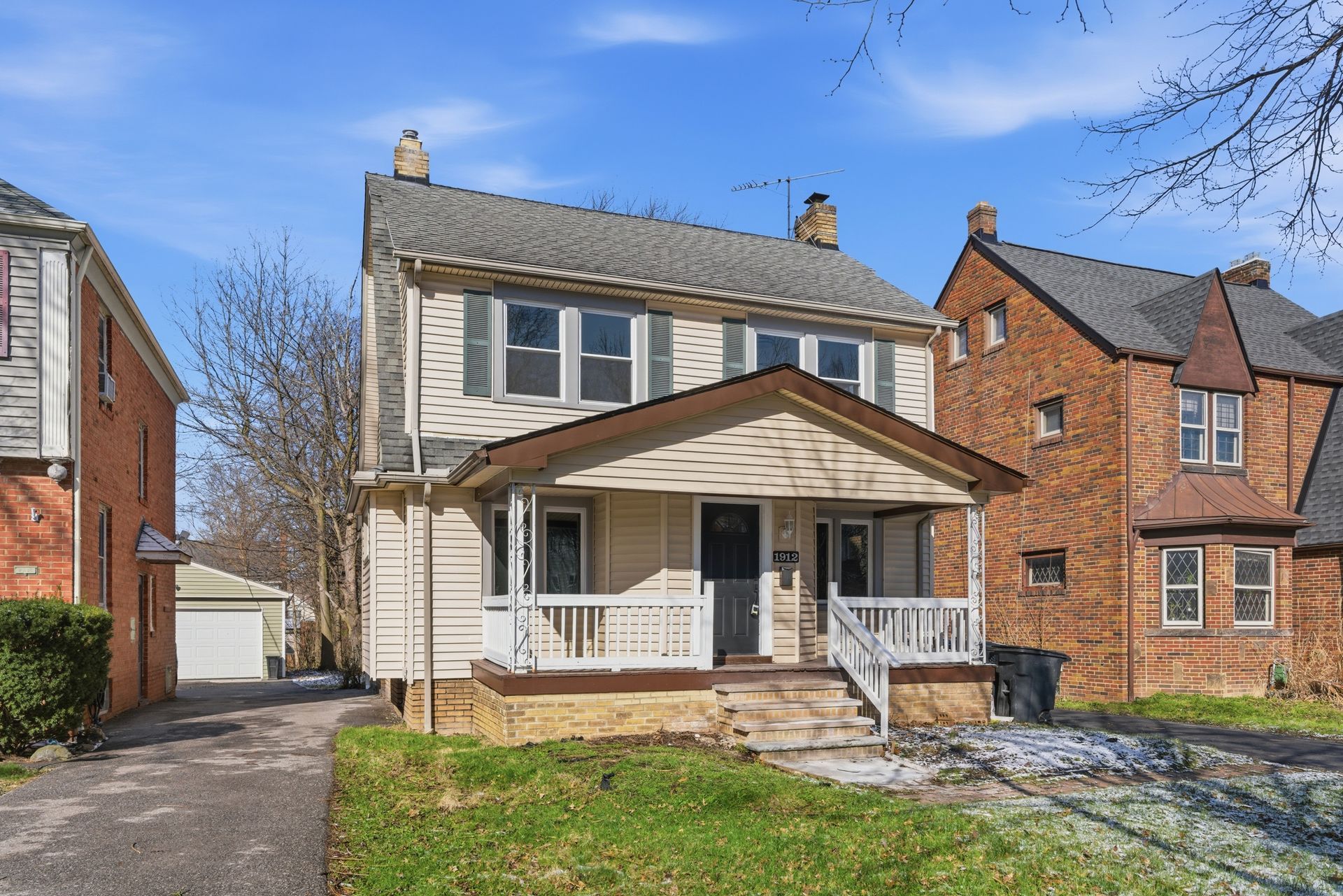 Two-story suburban house with white porch, driveway, and blue sky