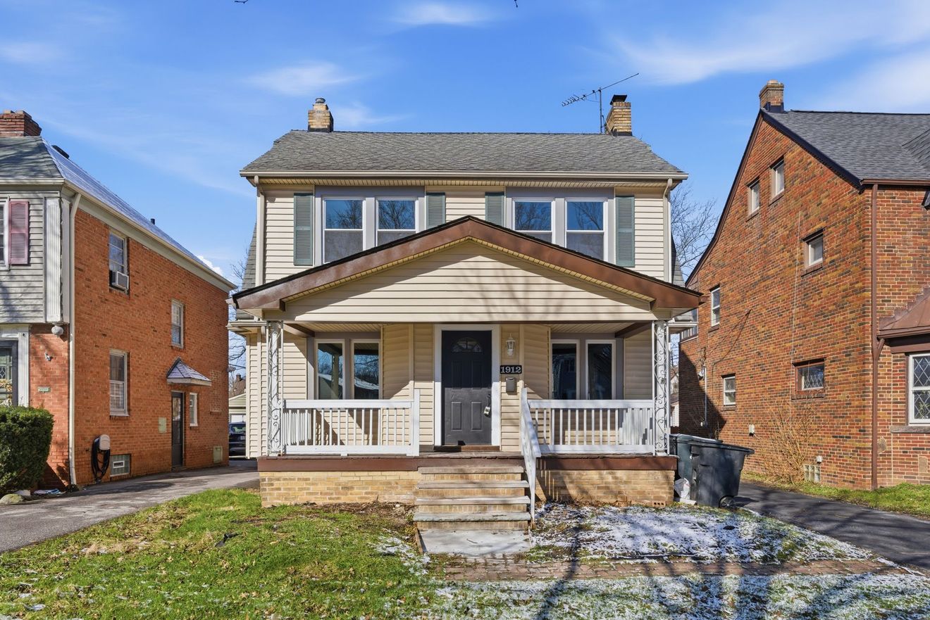 Front view of a two-story brick house with a covered porch and front steps under a blue sky