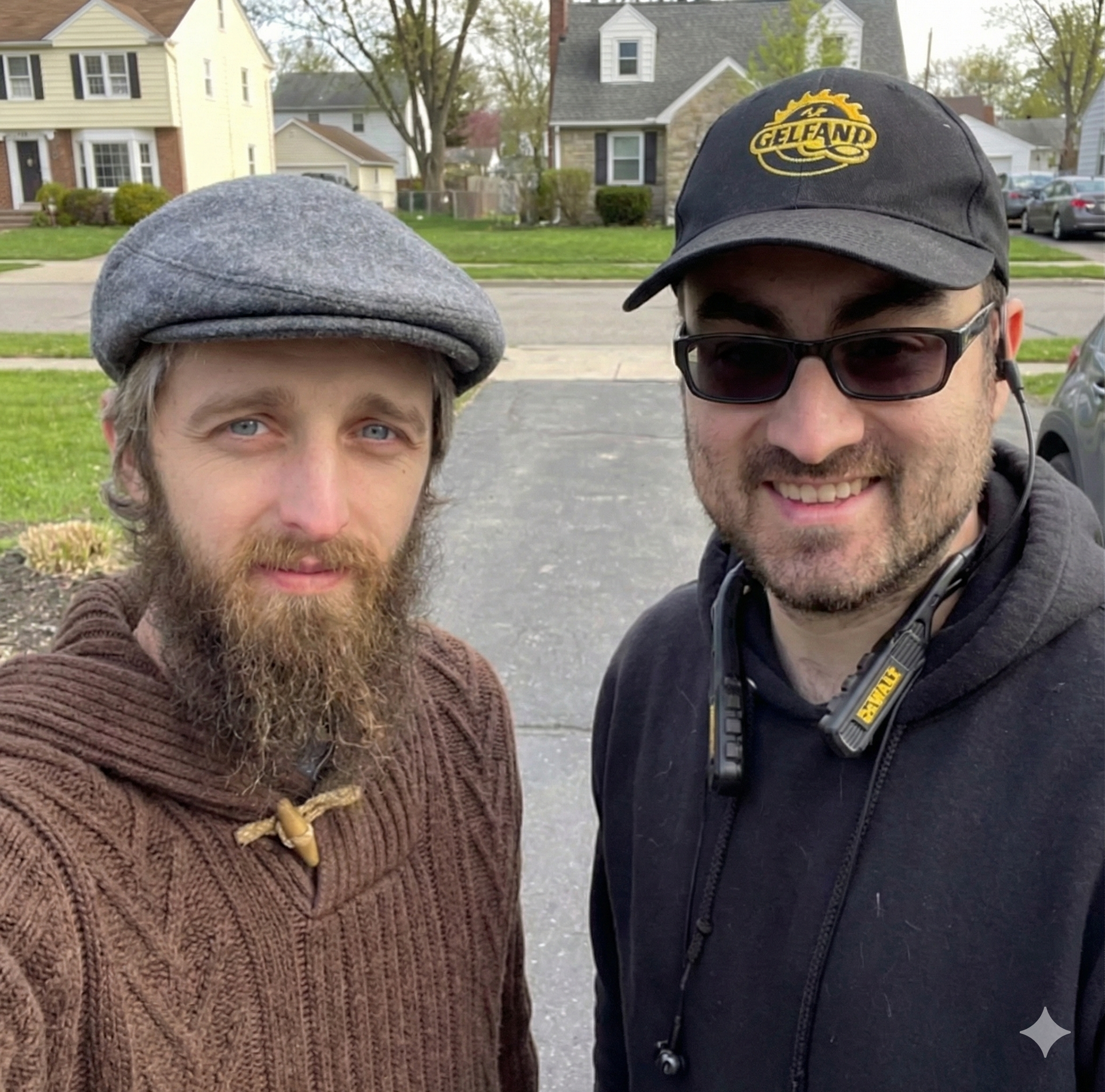 Two men smiling outdoors in a suburban neighborhood, one in a gray cap and one in black sunglasses and cap.