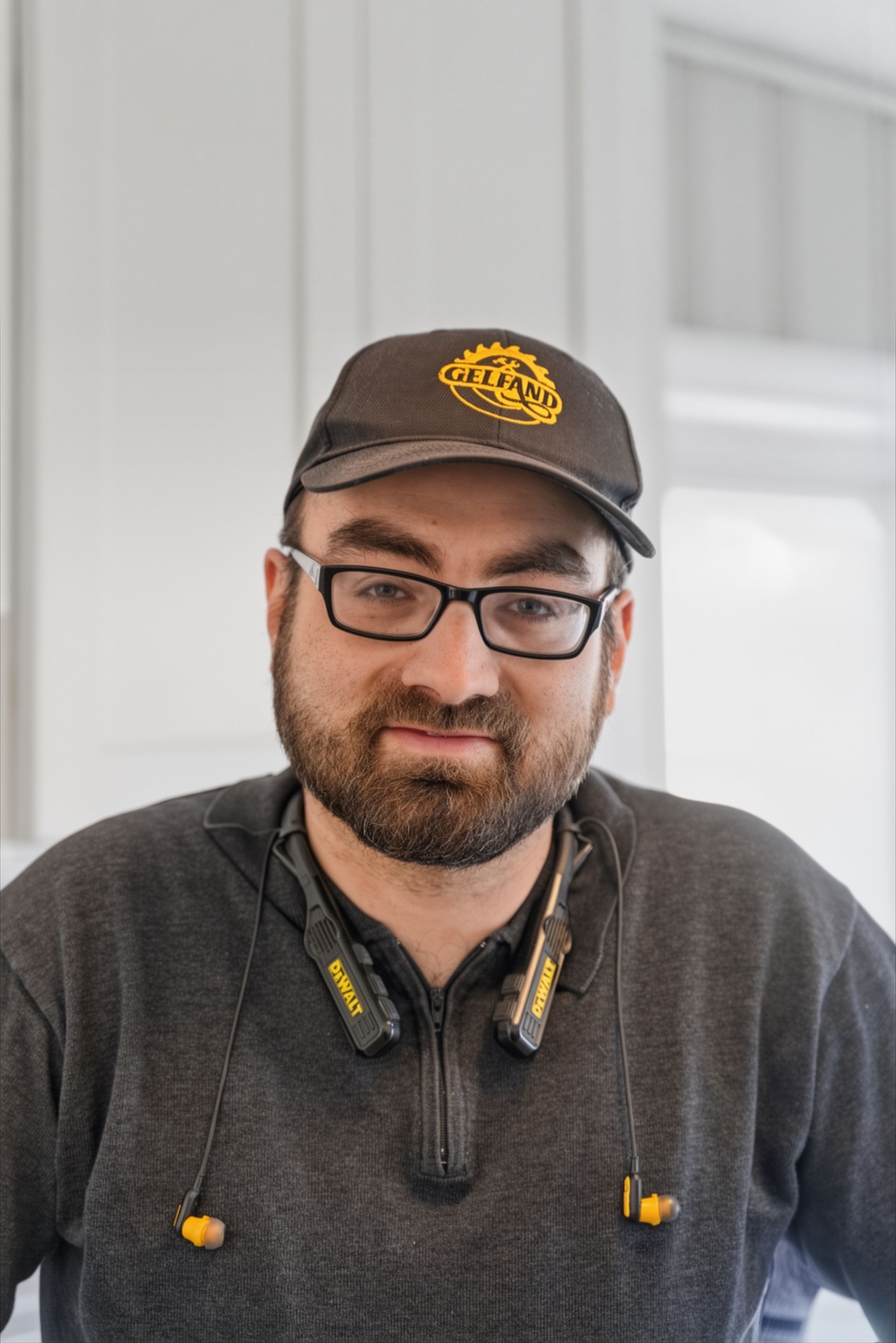 Man seated on indoor stairs, wearing a cap and glasses, smiling at the camera