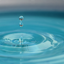 Water droplets falling into still, blue water, creating ripples.