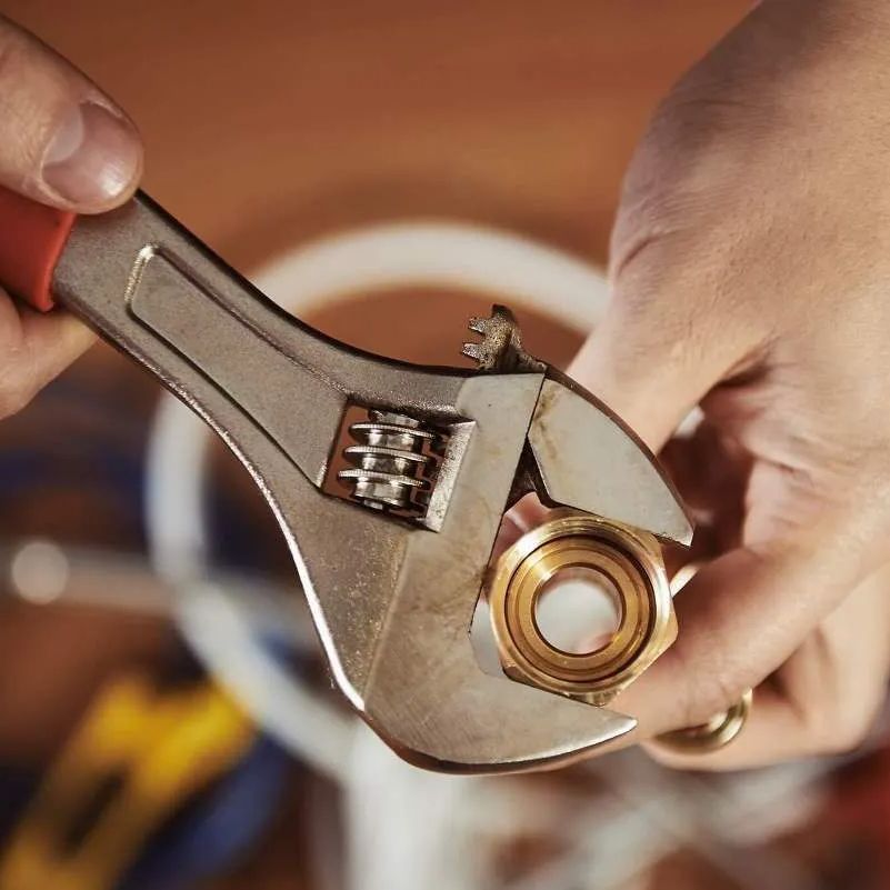 Hands using a wrench to tighten a brass fitting.