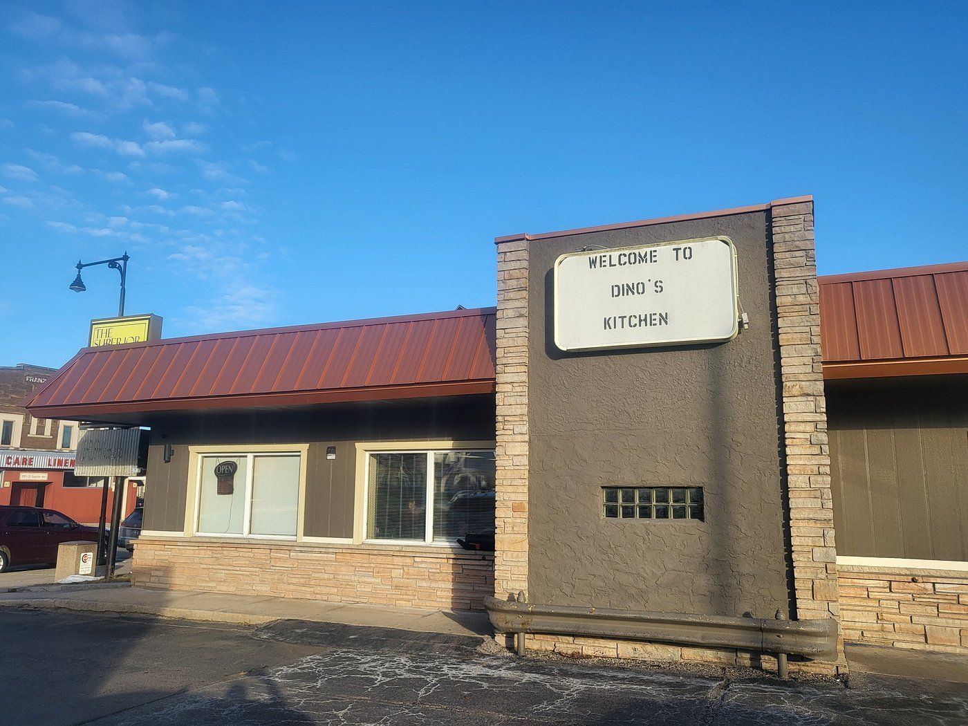 Brick storefront with a red roof and central sign under a clear blue sky