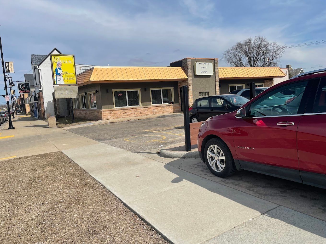 Parking lot outside a low brick building with a yellow roof and a red car in the foreground