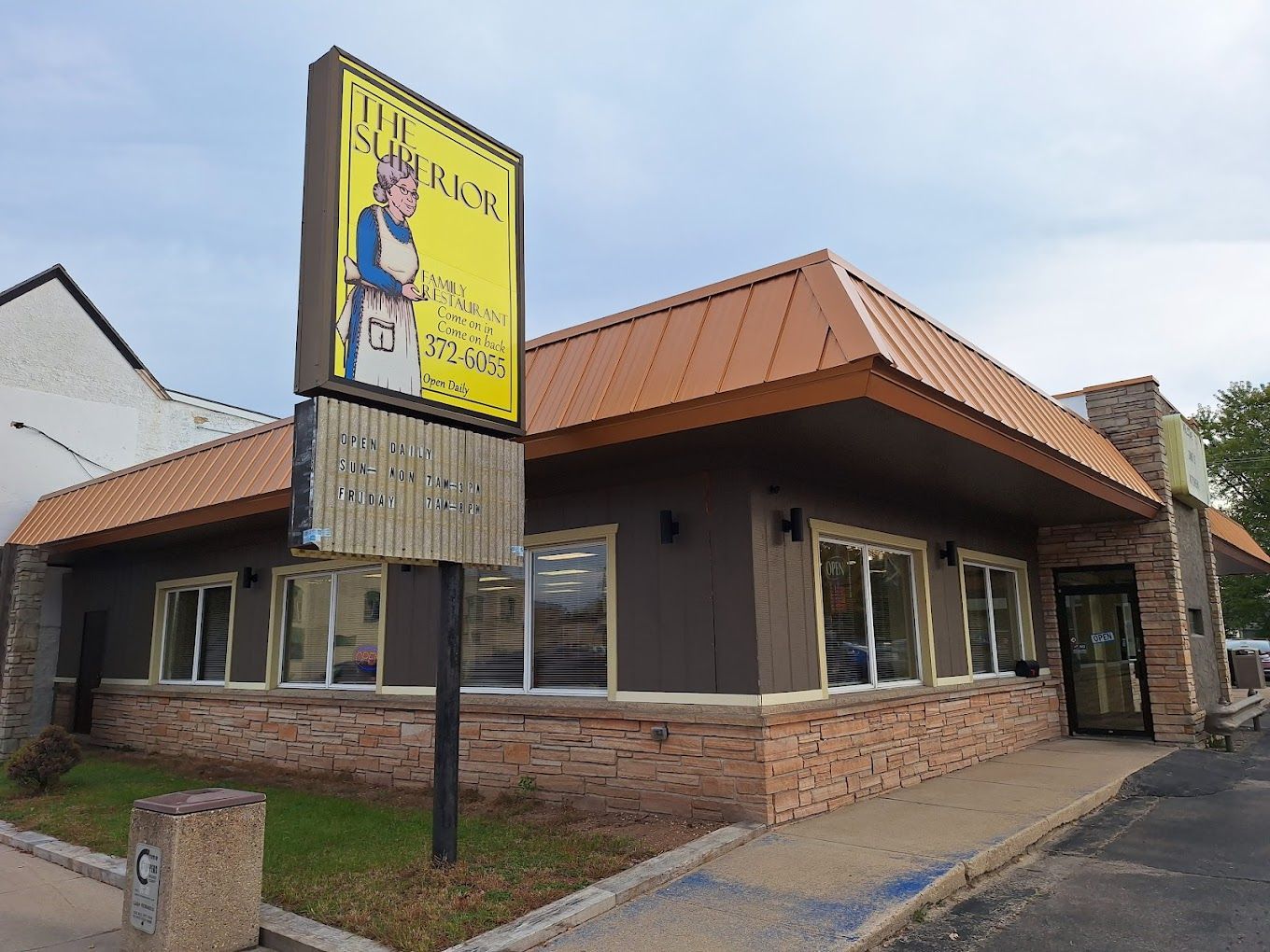 Brick commercial building with copper roof and yellow sign by the street.