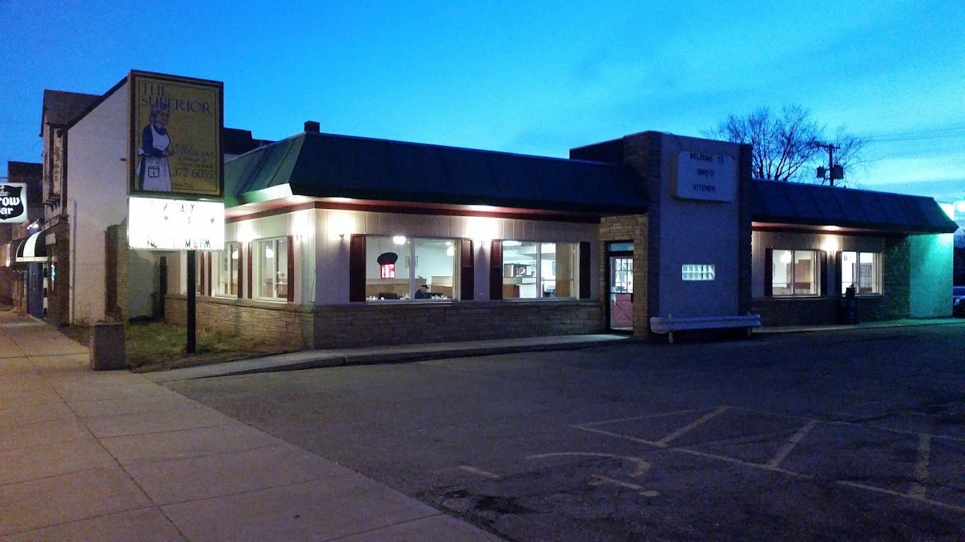 Small storefront at dusk with lit windows, a sign, and an empty parking lot.