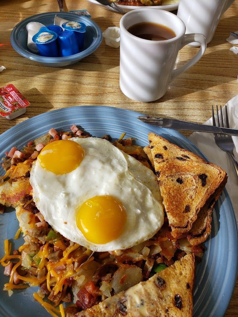 Blue plate with fried eggs on toast, hash browns, and coffee on a wooden table