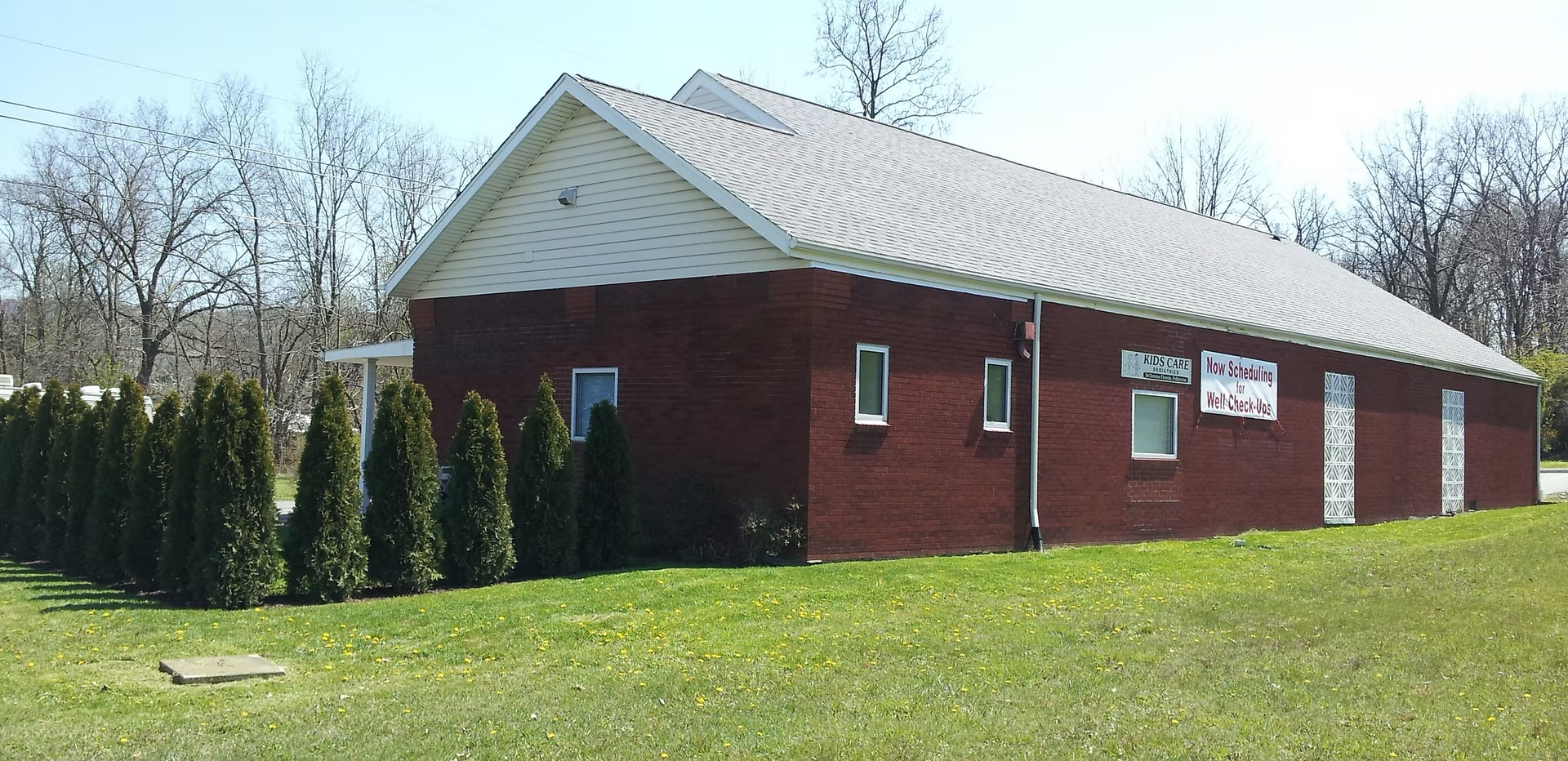 A red brick building with a white roof sits in the middle of a grassy field.