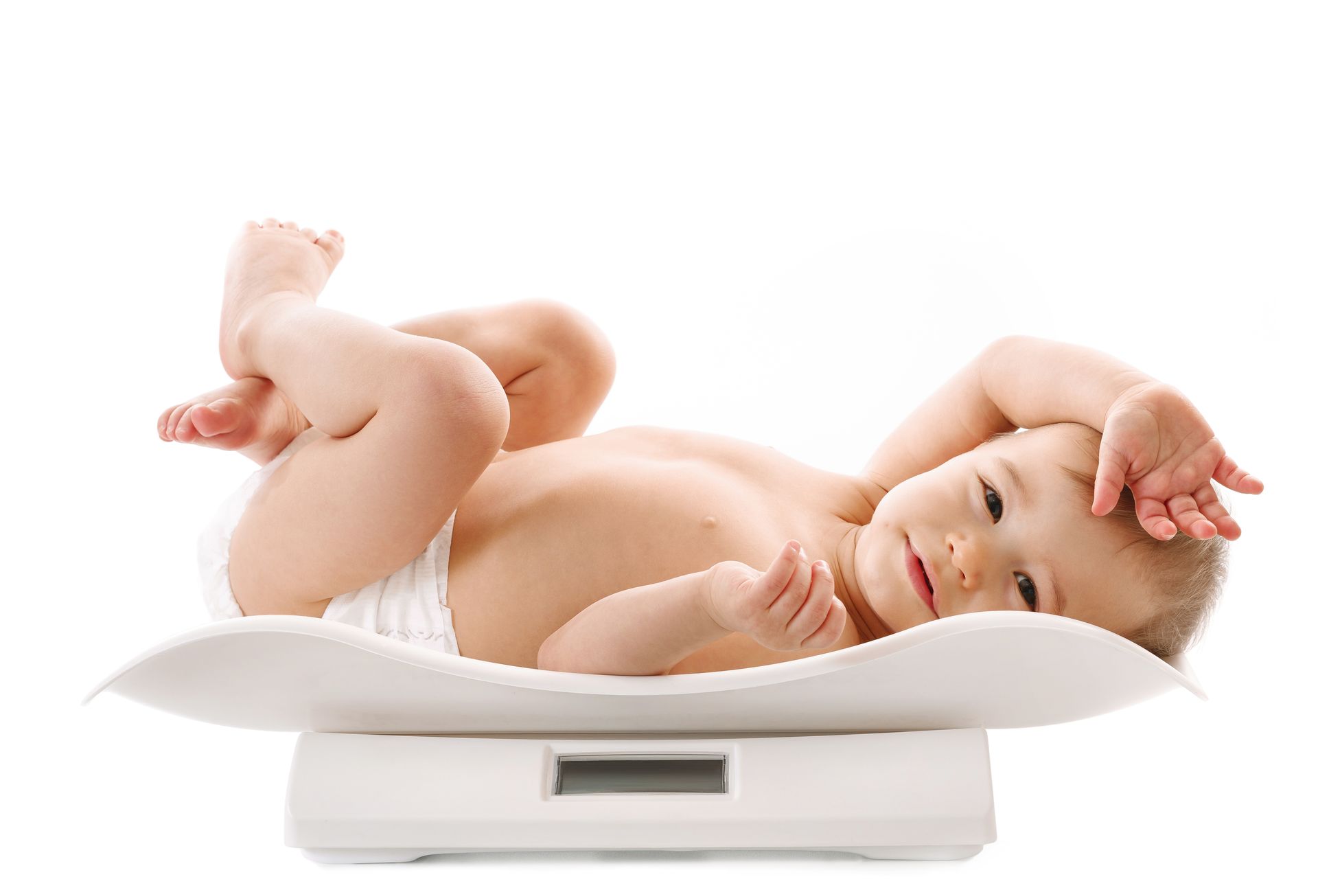 A baby in a diaper is laying on a scale.