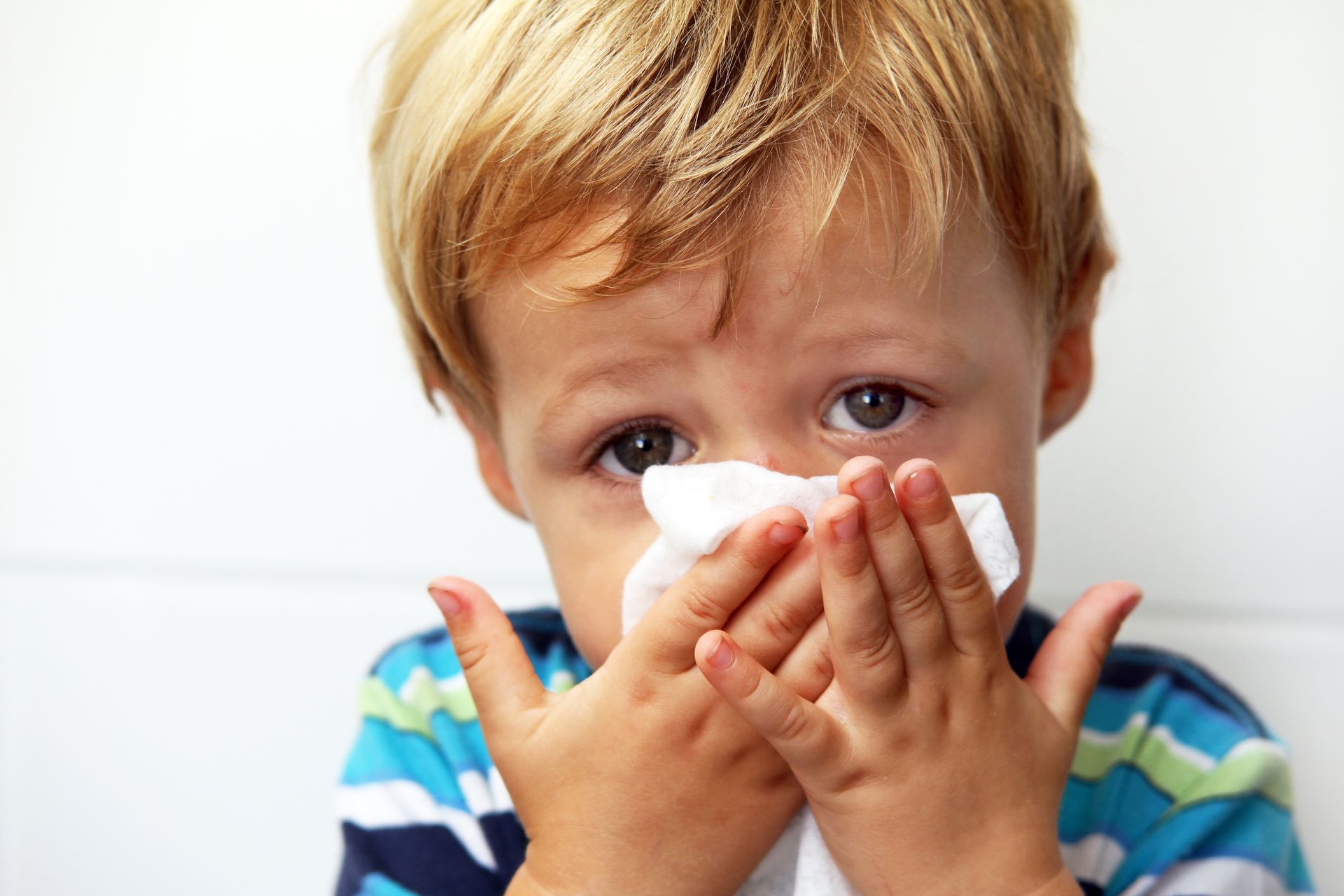 Young boy holding a kleenex over his nose.