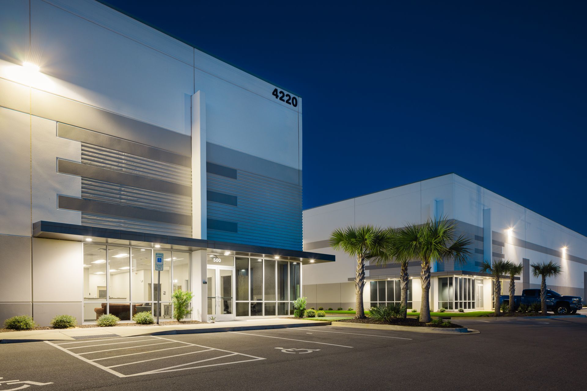 A large building with a parking lot in front of it at night.