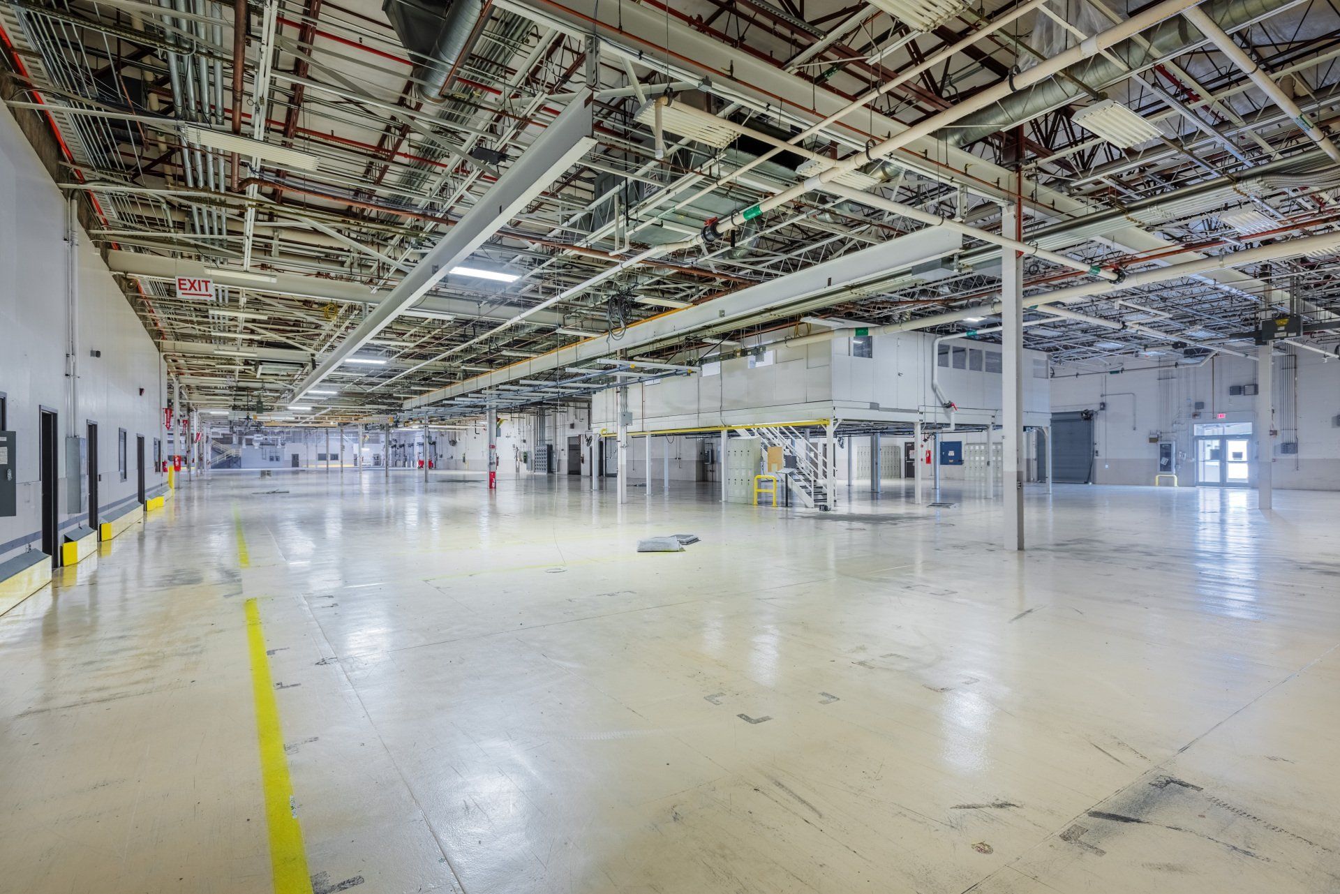 A large empty warehouse with a lot of pipes hanging from the ceiling.