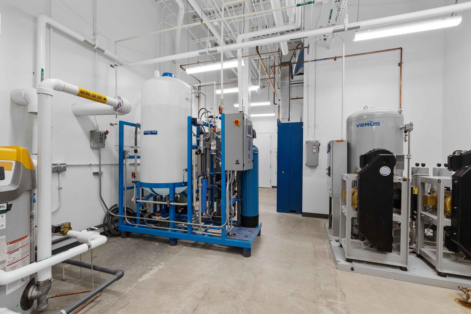 Utility room with industrial water treatment equipment, including large tanks and blue metal frames on a concrete floor.
