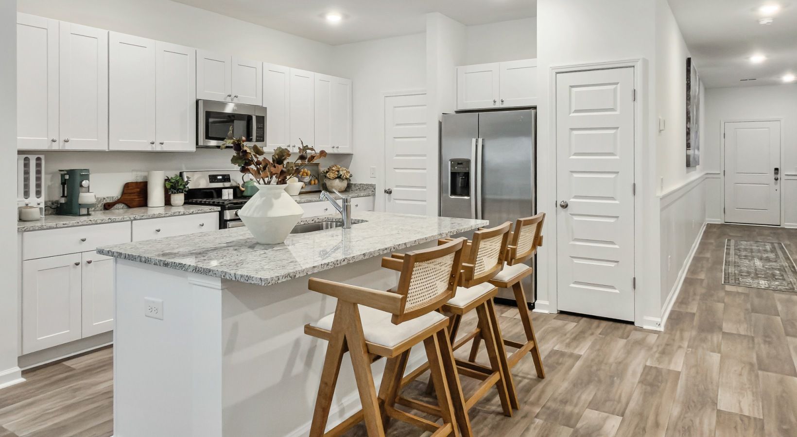Modern white kitchen with island, stainless steel appliances, and hardwood floors.