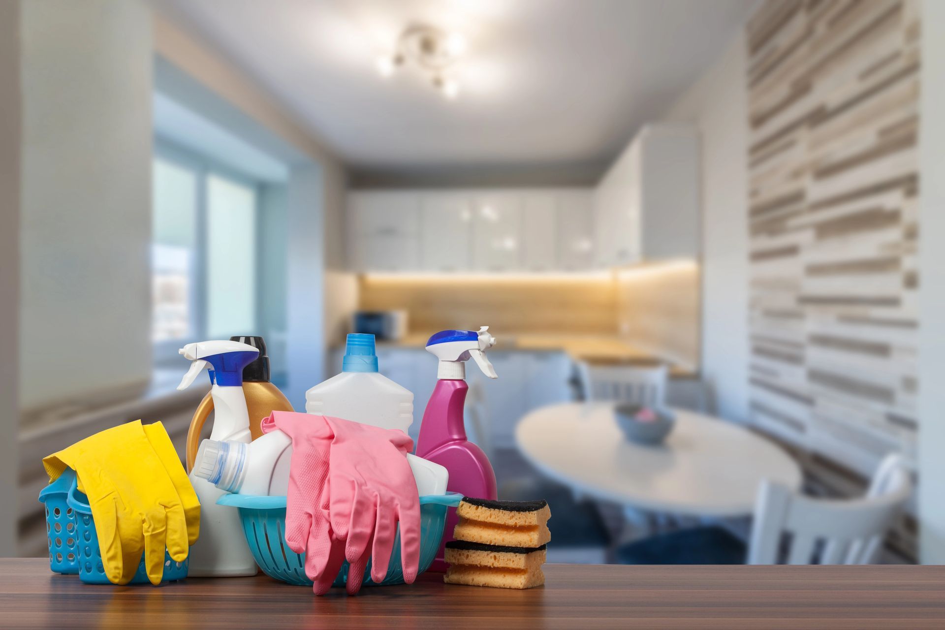 Prodotti per la pulizia colorati su un bancone in una cucina o sala da pranzo luminosa e moderna.