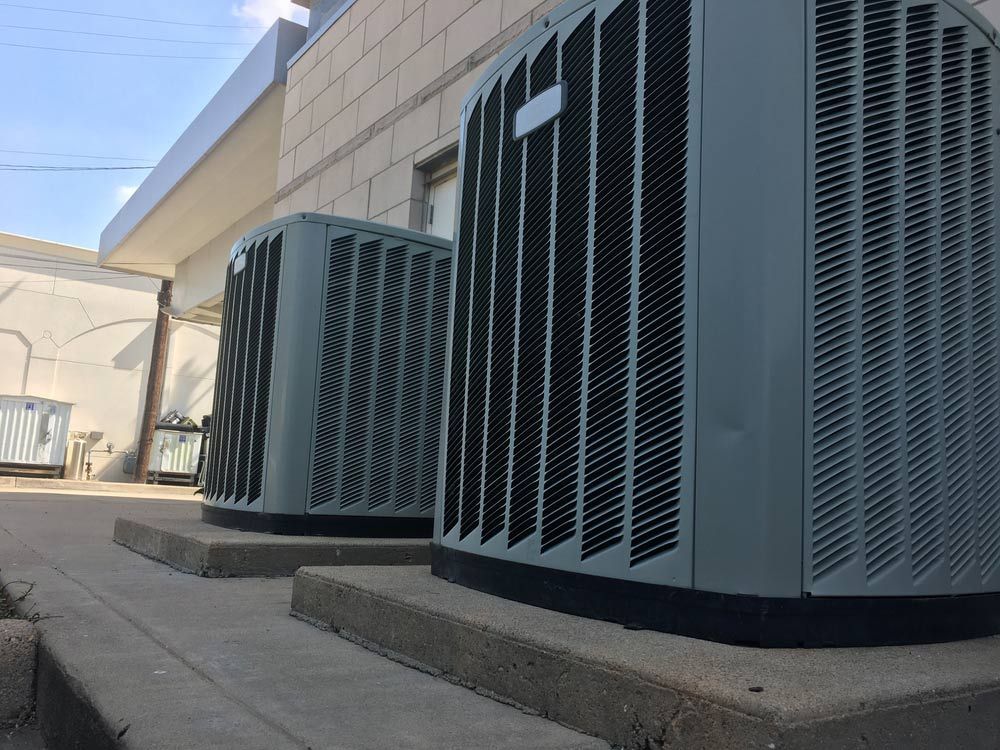 Two Air Conditioners Are Sitting On The Sidewalk Outside Of A Building — Priest Airconditioning in Ashmont, NSW