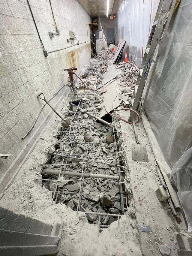 Narrow demolition trench with broken concrete, exposed rebar, and debris between tiled walls