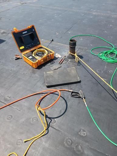 Orange test case with cables and a coiled green wire on a dark floor, beside a black cylinder and tools