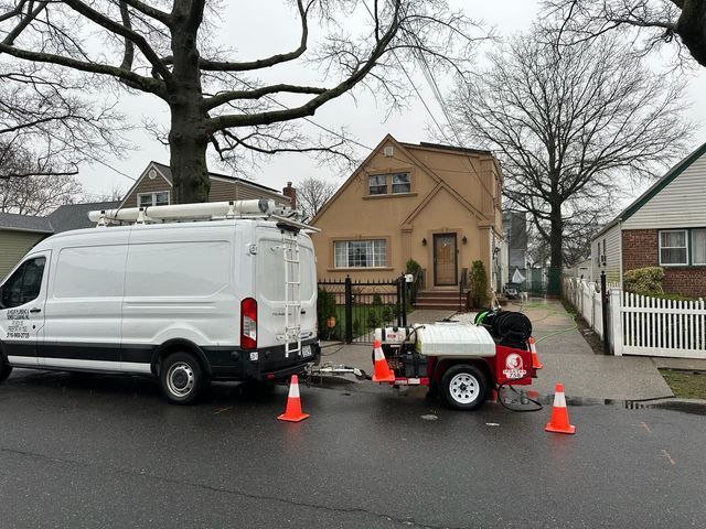 Worker and white van on wet residential street with cones and portable equipment