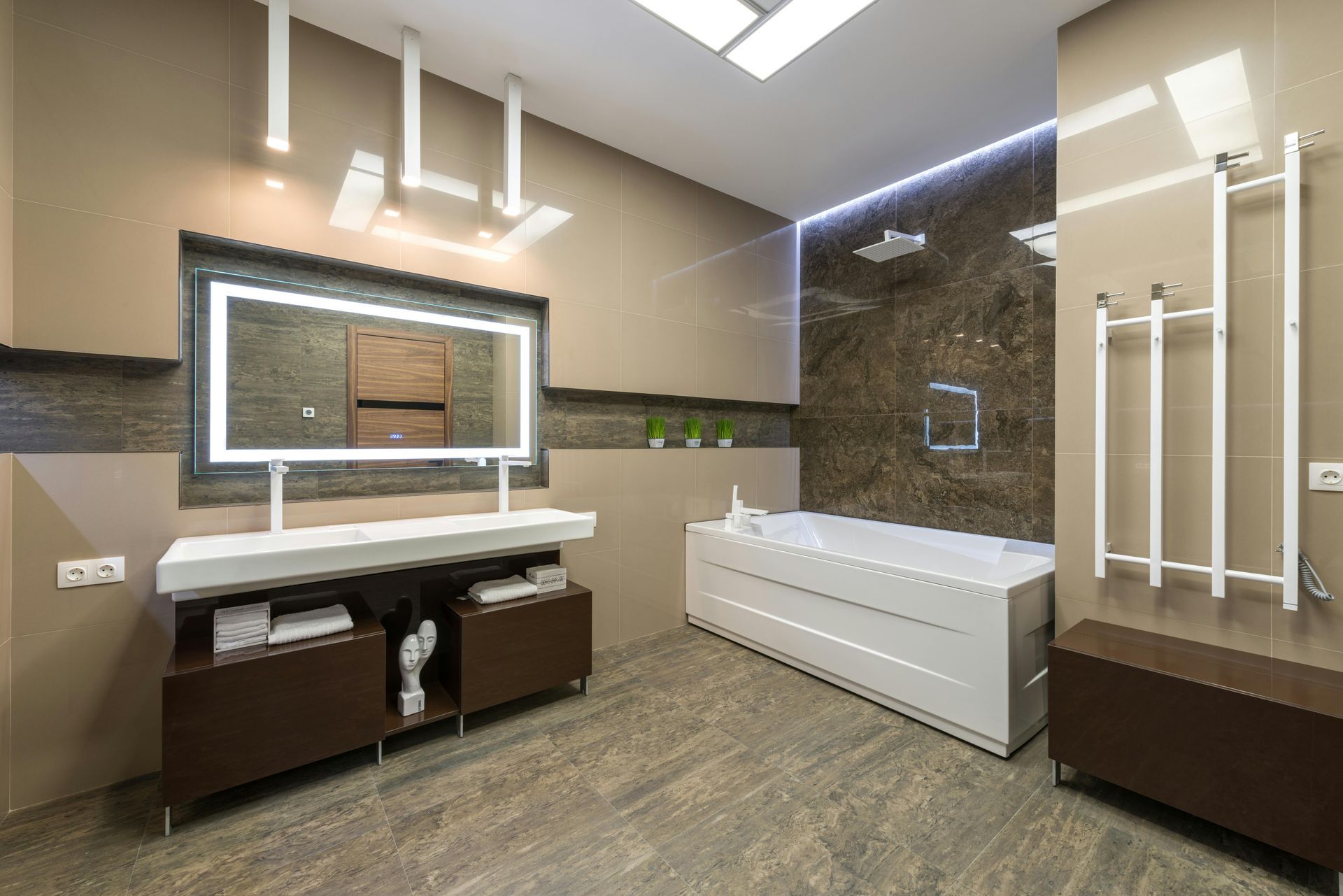 Modern, neutral-toned bathroom with a backlit mirror, white floating vanity, soaking tub, and vertical towel rack.