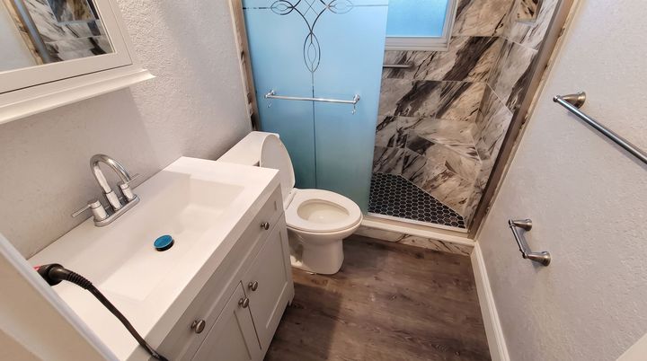 Small bathroom with toilet, sink cabinet, towel rail, and blue door in a narrow space