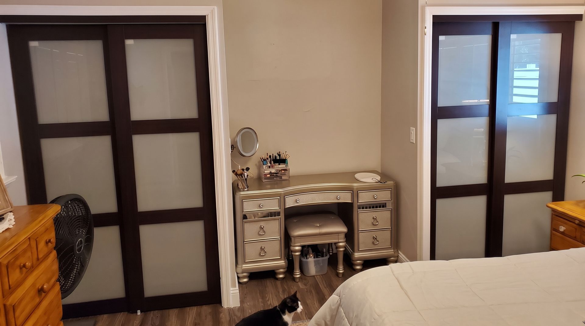 Bedroom with a mirrored vanity centered between two dark-framed doors and a bed in the foreground