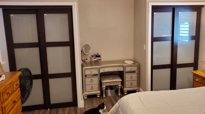 Bedroom with a mirrored vanity centered between two dark-framed doors and a bed in the foreground