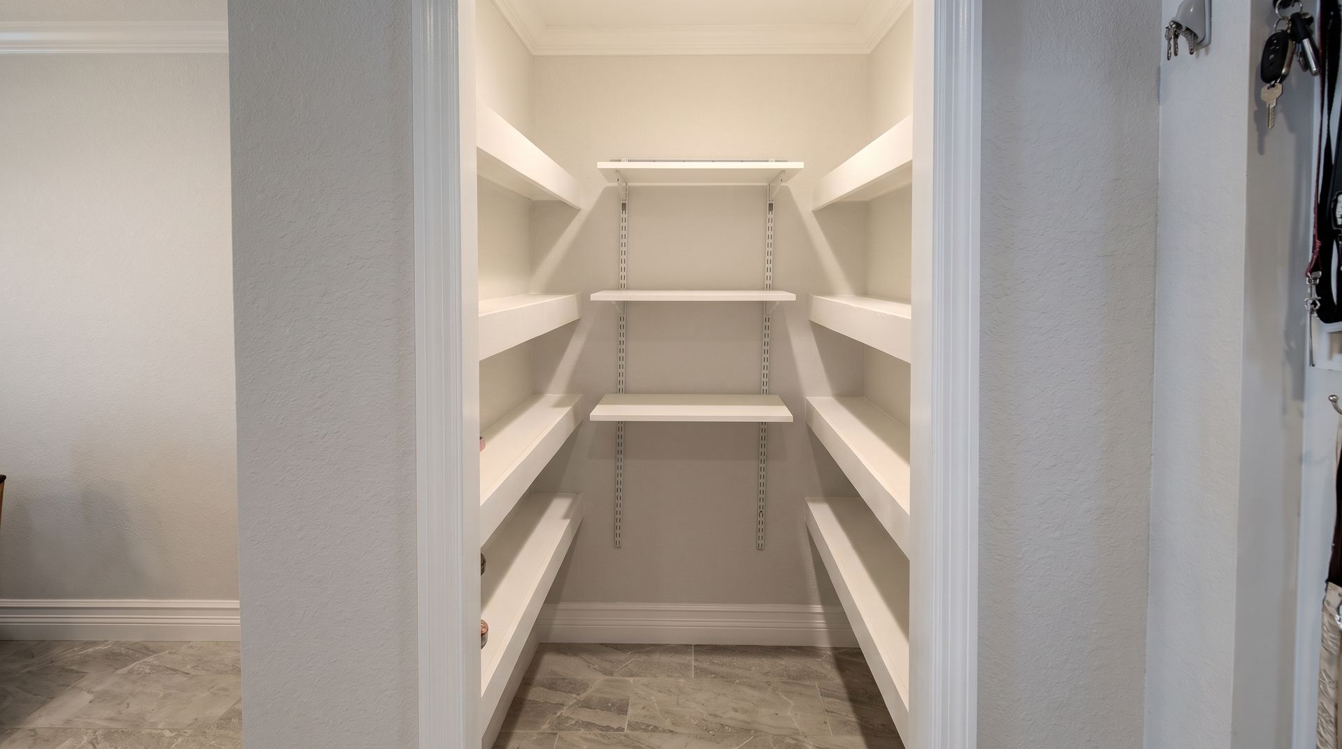 Empty white walk-in pantry with built-in shelving on both sides and back wall.