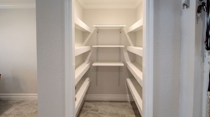 Empty white walk-in pantry with built-in shelving on both sides and back wall.