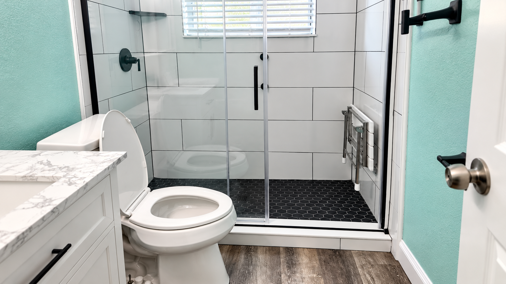 Bathroom with white vanity, toilet, and glass-enclosed shower with black tile floor.