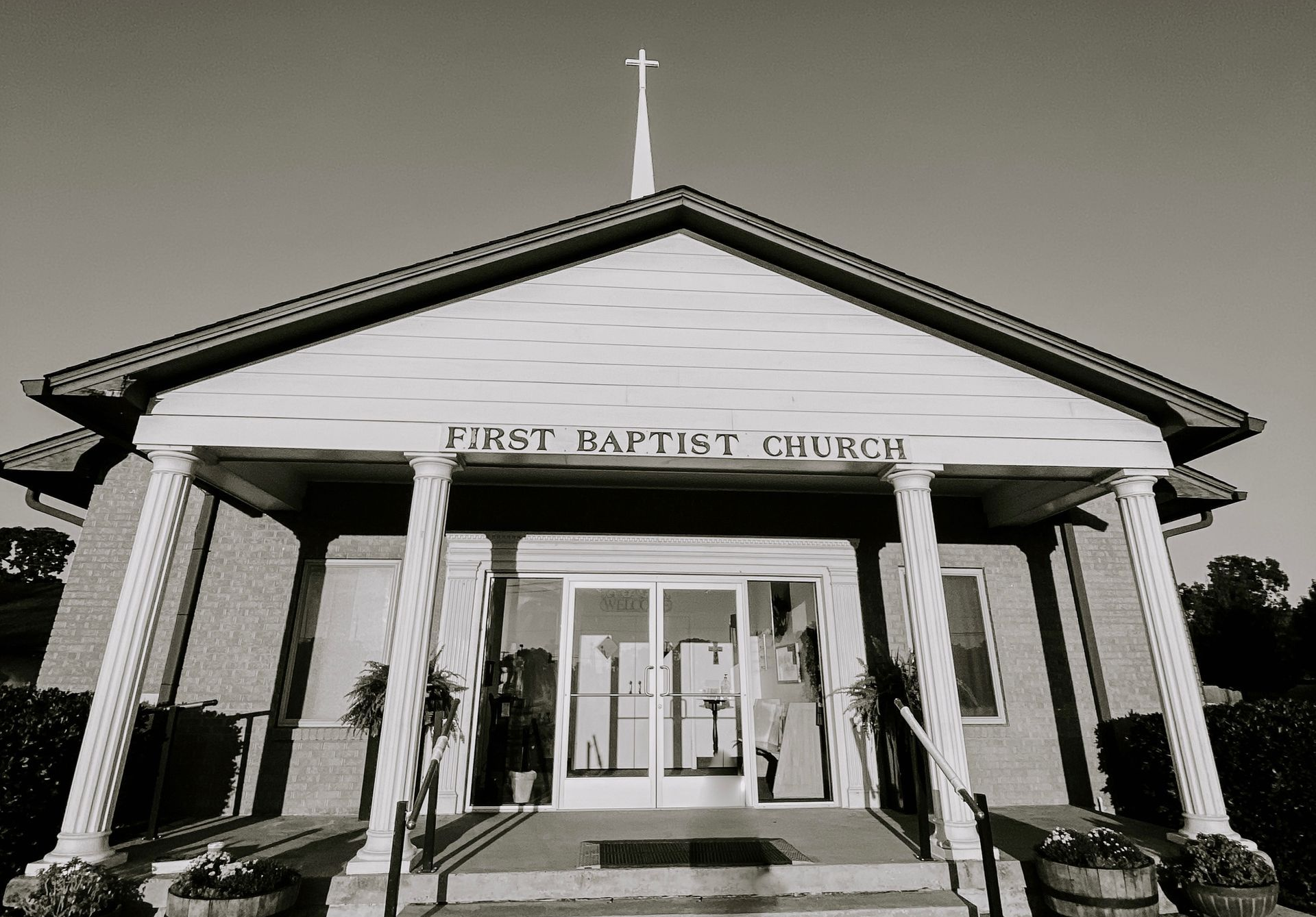 Front view of a church with a white facade, columns, and cross-topped steeple
