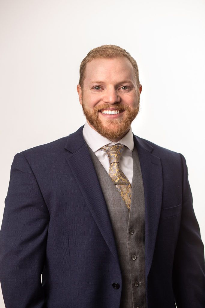 Smiling pastor in a navy suit, vest, and tie against a light background