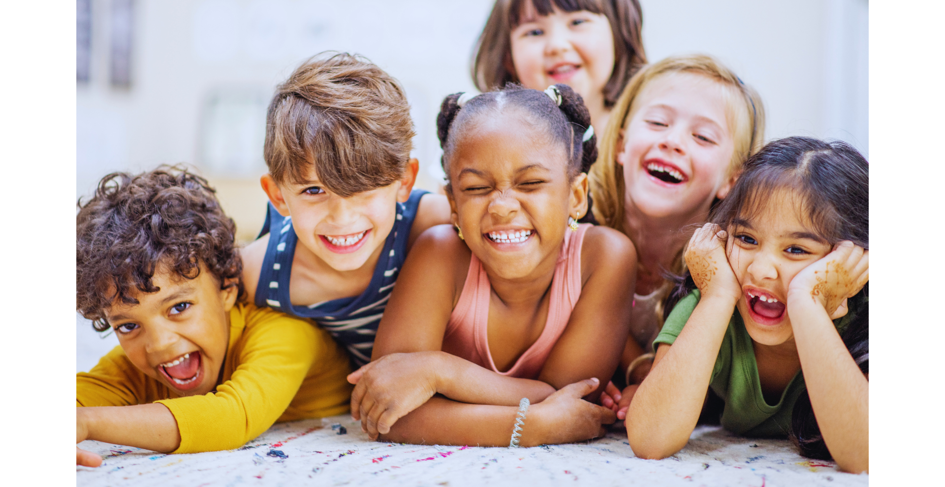 Five children lying on the floor, smiling and laughing at the camera.