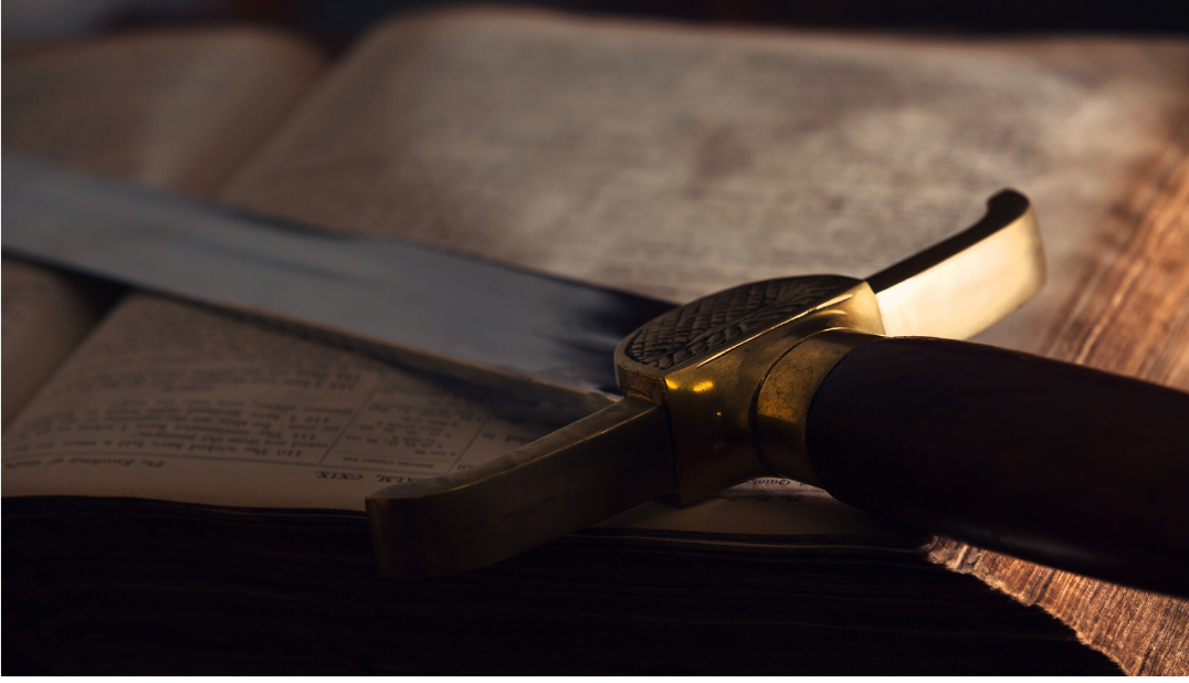 A sword resting on an open book, with warm light reflecting on the blade and pages.