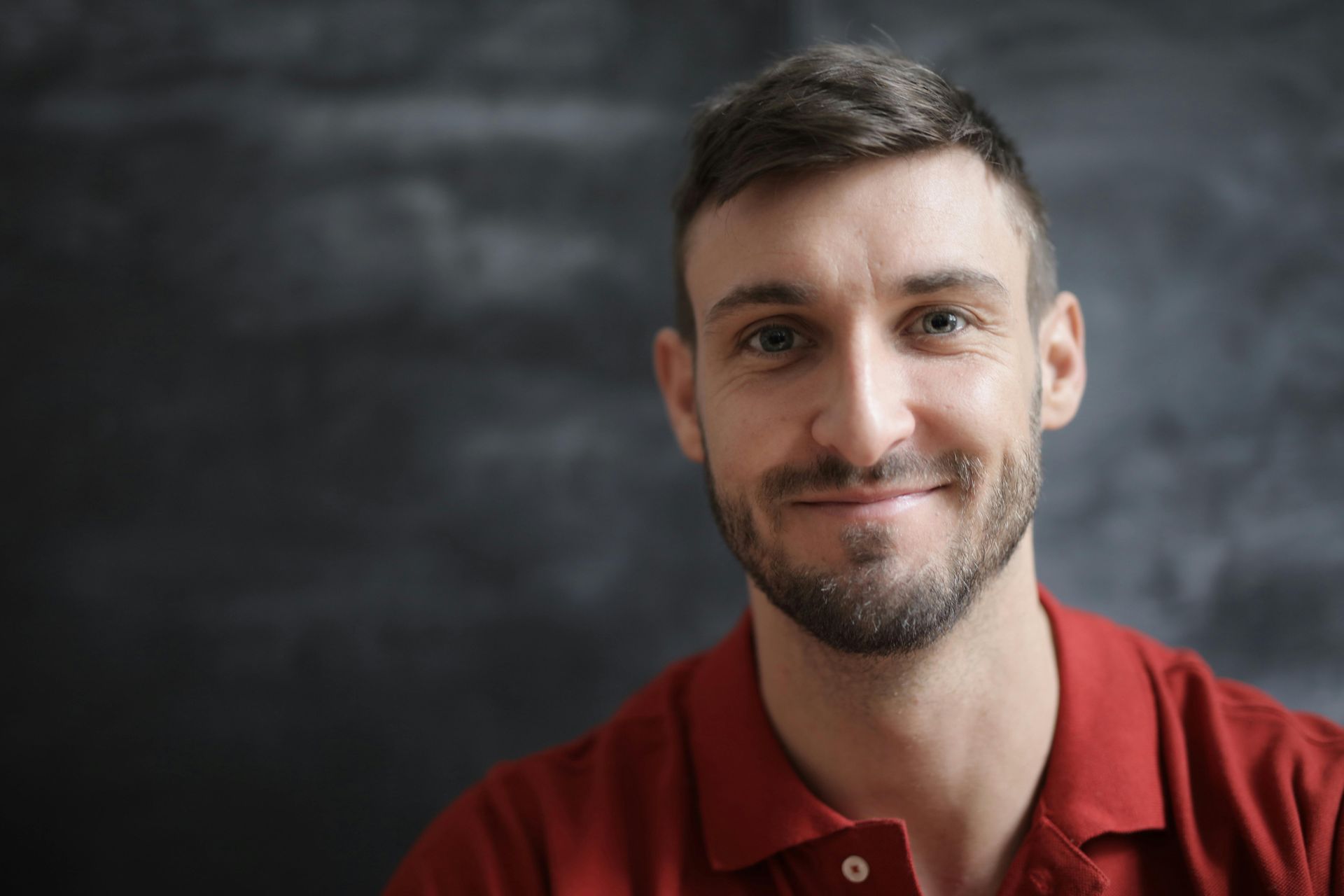 Smiling man in a red shirt against a dark, blurred background
