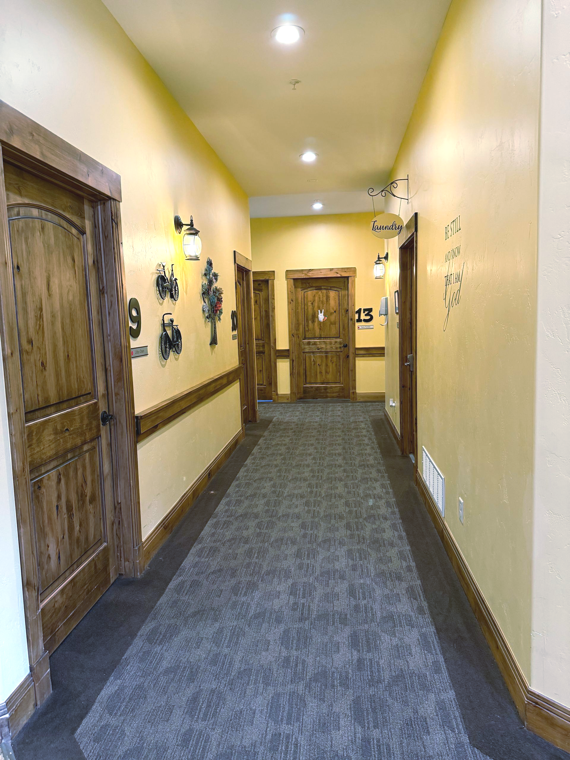 Long hallway with gray carpet, yellow walls, and wooden doors.