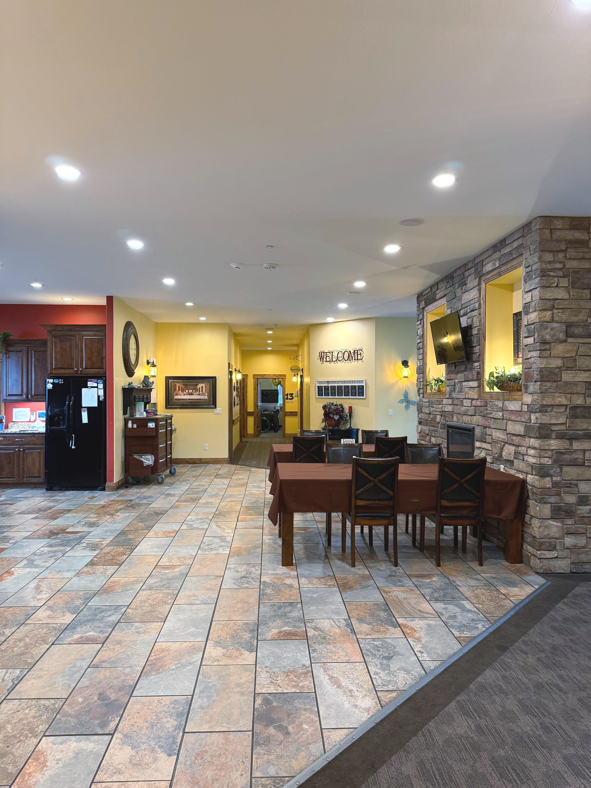 A dining area in a senior living facility, with tables, chairs, and stone accent wall.