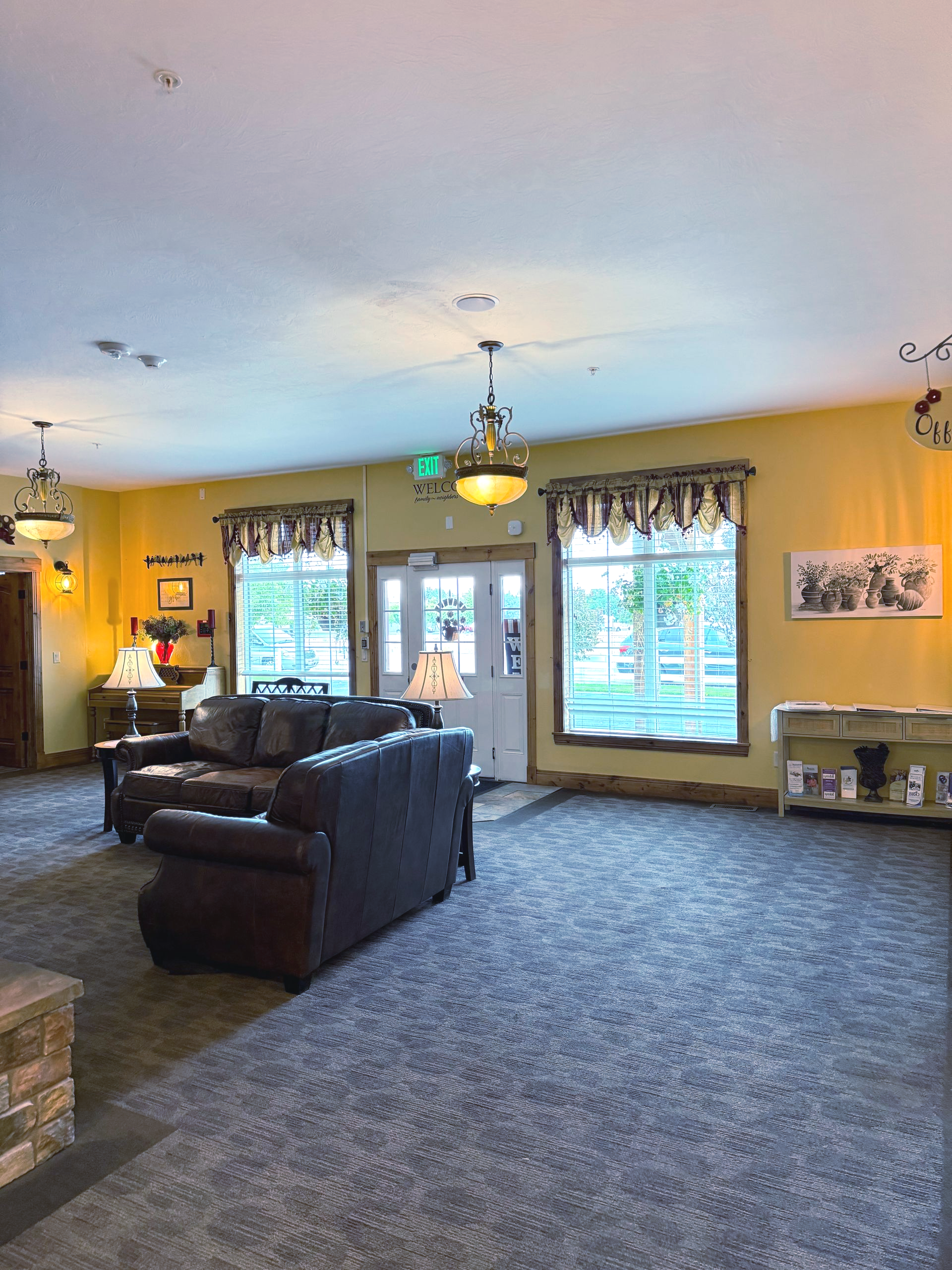 Lobby with brown sofas, yellow walls, and large windows. Dark gray carpet and vintage light fixtures.