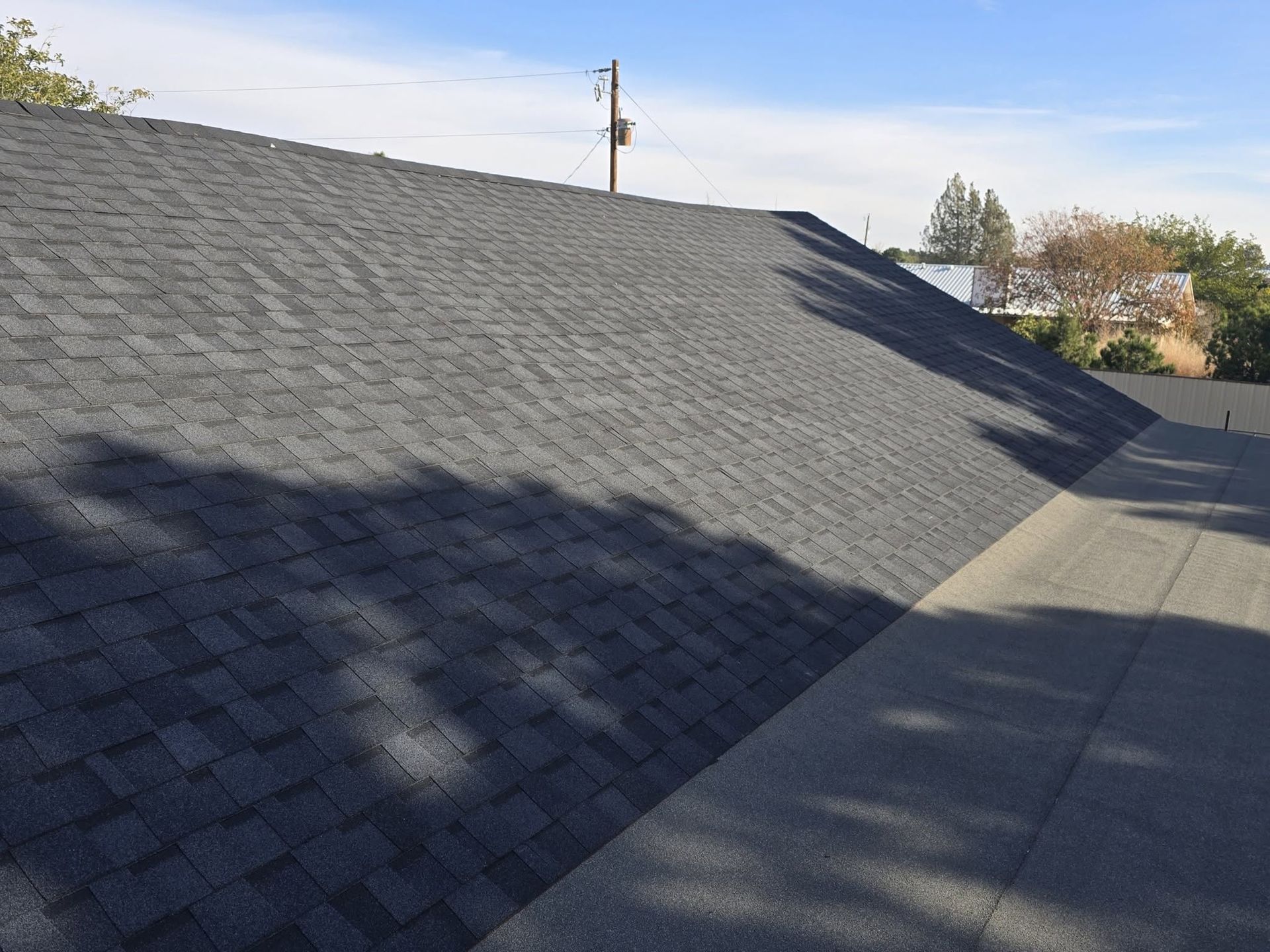 Gray shingle roof with shadows beside a concrete walkway under a clear sky