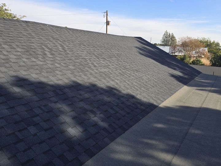 Gray shingle roof with shadows beside a concrete walkway under a clear sky