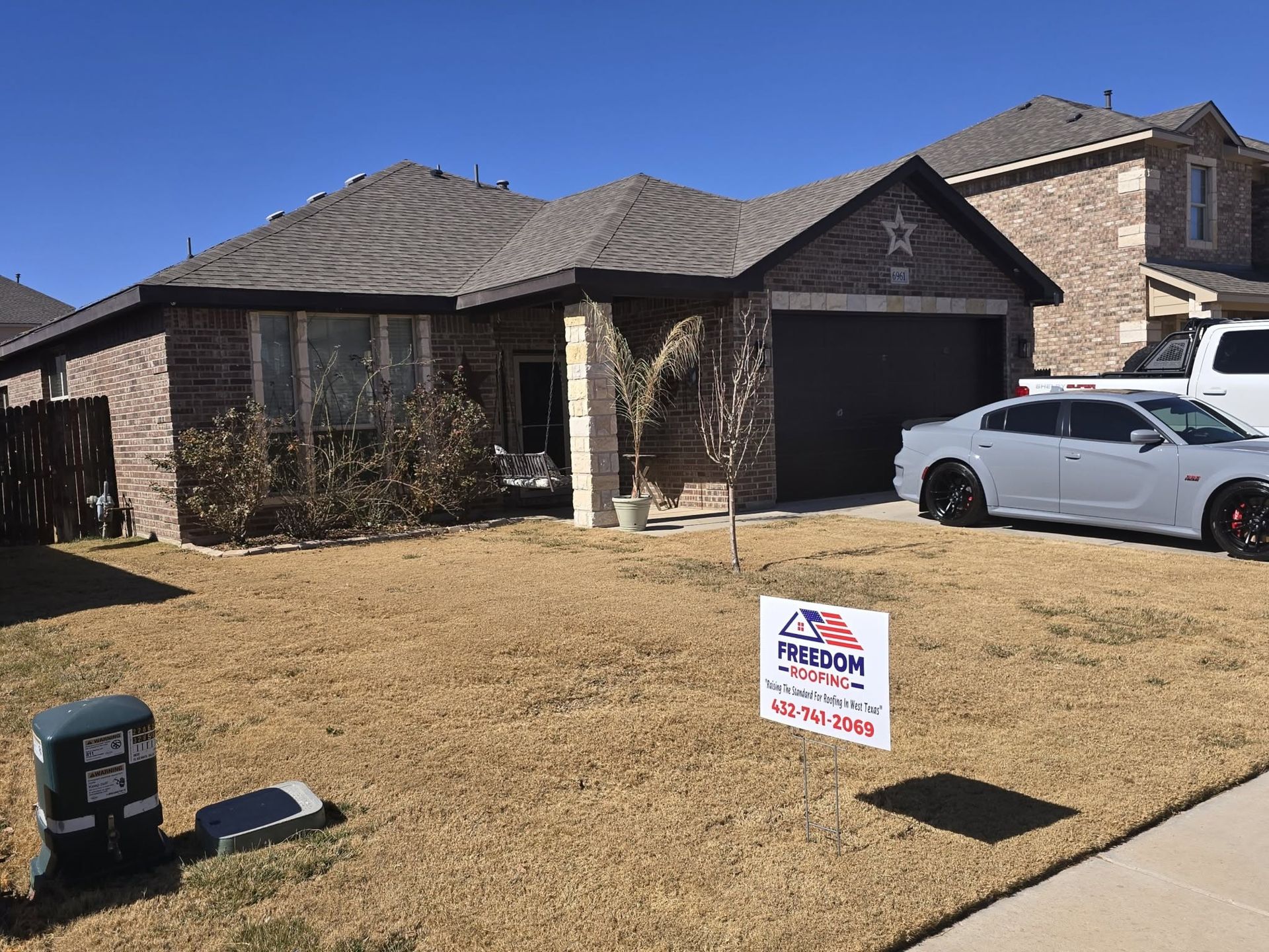 Suburban brick house with a white car in the driveway and a yard sign on the lawn