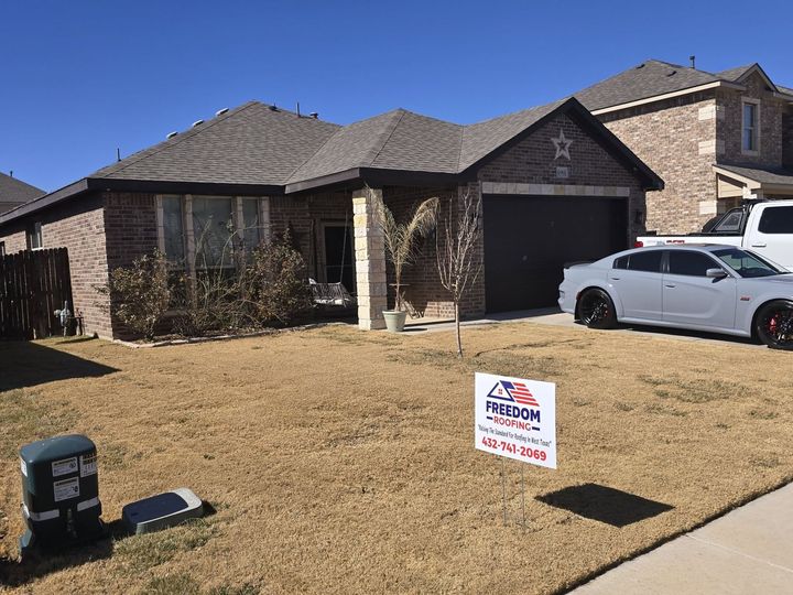 Suburban brick house with a white car in the driveway and a yard sign on the lawn